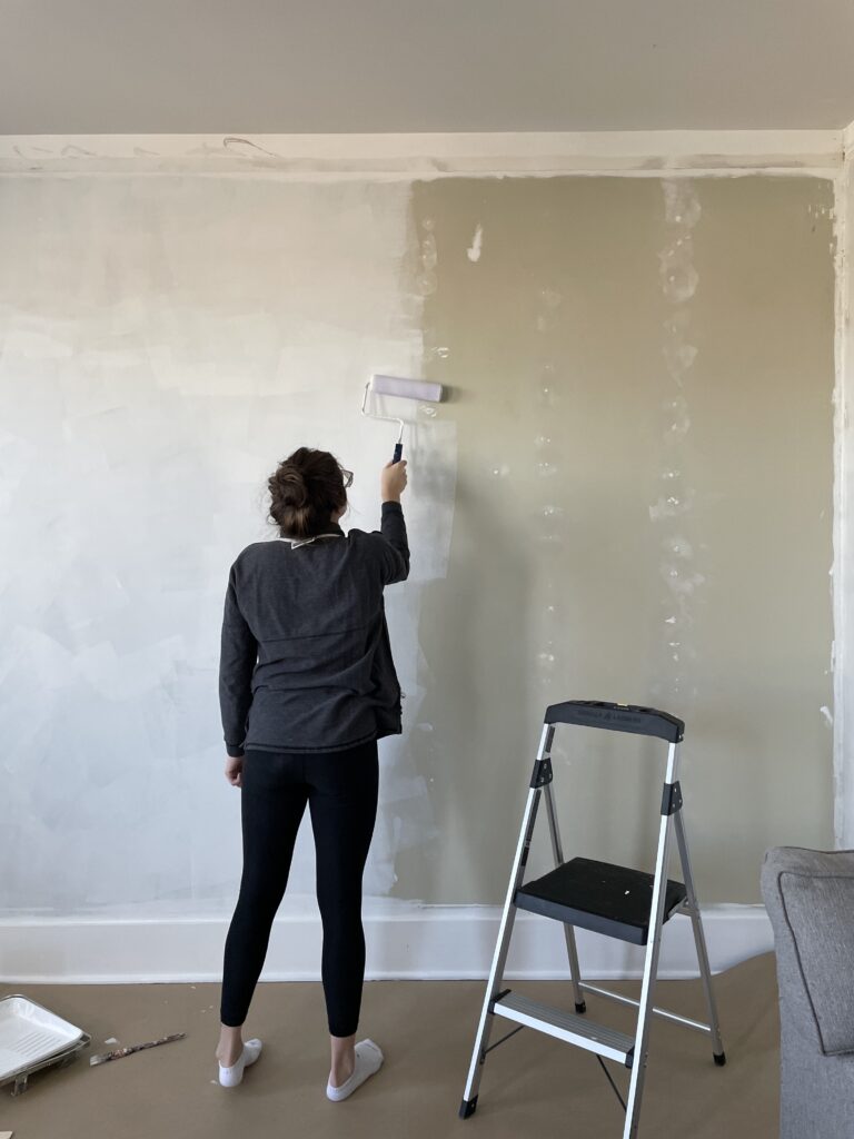 Elisha from Our Aesthetic Abode is priming a green wall with a roller brush before she starts on the recessed wainscoting accent wall