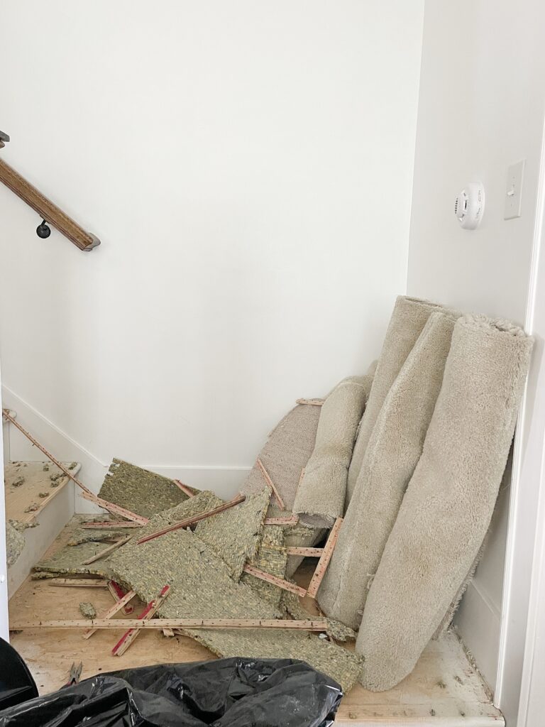 Piled up carpet, tack strips, and foam pad resting on a stair landing after being removed