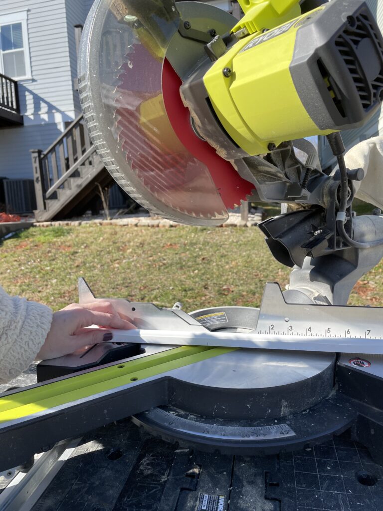 Elisha from Our Aesthetic Abode is using her miter saw to cut an angle on a piece of trim. The miter saw is #4 of her beginner DIYer checklist