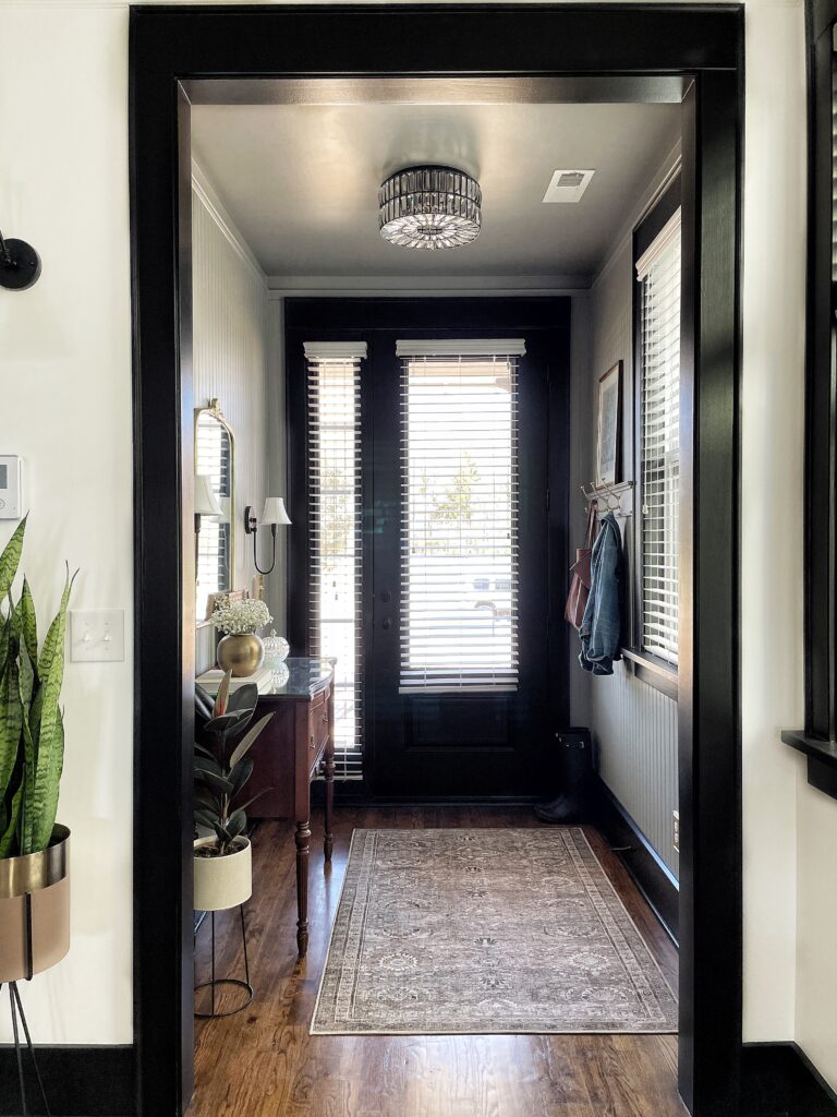 Elisha from Our Aesthetic Abode's finished beadboard entryway makeover. It's greige with black trim, a crystal flush mount, a vintage vanity with a mirror above and black sconces on each side of the mirror. 