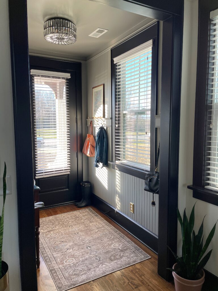 A view of Elisha from Our Aesthetic Abode's beadboard entryway makeover featuring her beautiful custom trim with oversized brass hooks