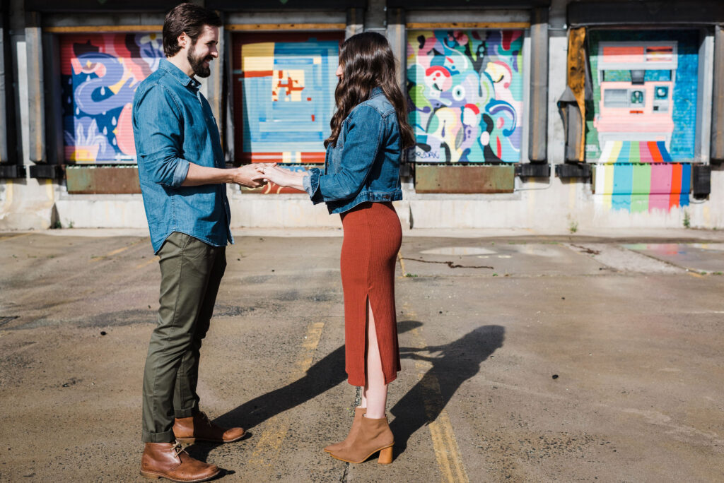 Elisha and Dan from Our Aesthetic Abode are facing each other and holding hands.

Elisha is wearing a jean jacket, a rust colored midi skirt with a slit, and brown pointed toe booties.

Dan is wearing a denim button up shirt with olive chino pants and cognac chukka boots.