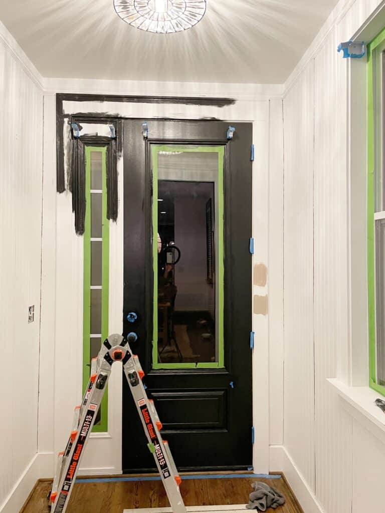 Elisha at Our Aesthetic Abode's beadboard entryway makeover in progress. Her front door is painted black and the trim surrounding it is partially painted black. It was originally white.