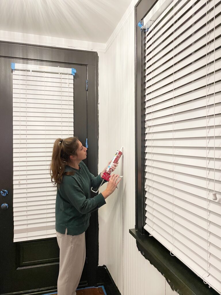 Elisha from Our Aesthetic Abode is caulking the seams where two beadboard panels meet for her beadboard entryway makeover