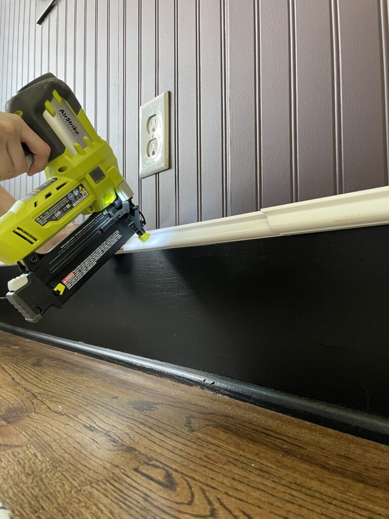 Elisha from Our Aesthetic Abode is using her brad nailer to install a trim piece above the baseboard for her beadboard entryway makeover