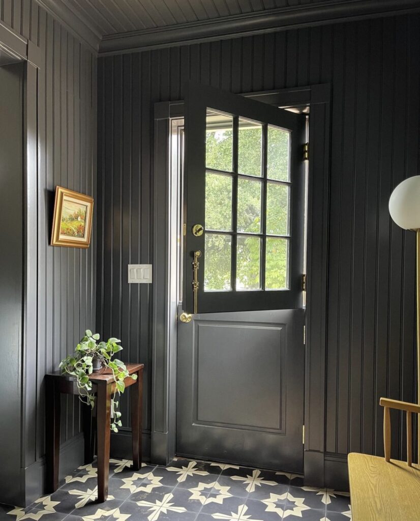 A moody entryway with floor to ceiling dark gray beadboard, wood and brass details, and a dutch door!