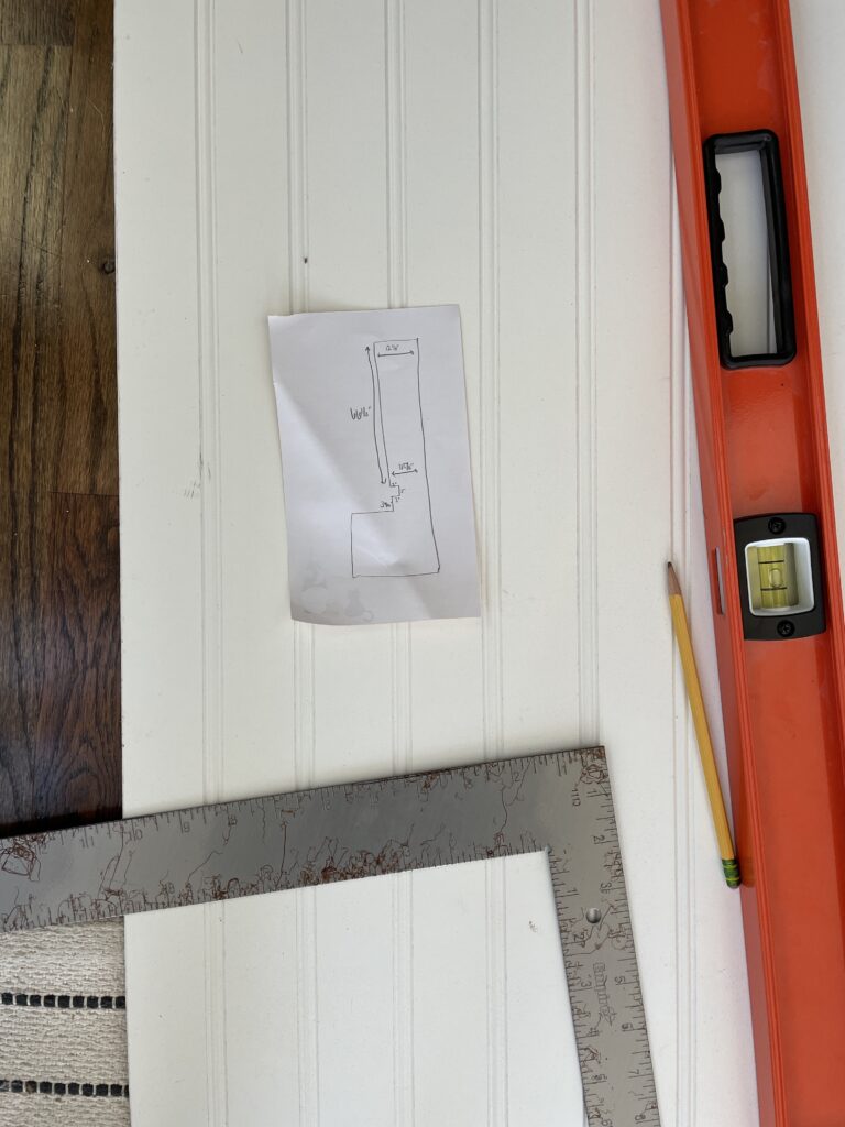 Beadboard, a carpenter's square, a large level, a pencil, and a sketch for a cut. The level is #8 on Elisha at Our Aesthetic Abode's Beginner DIYer checklist