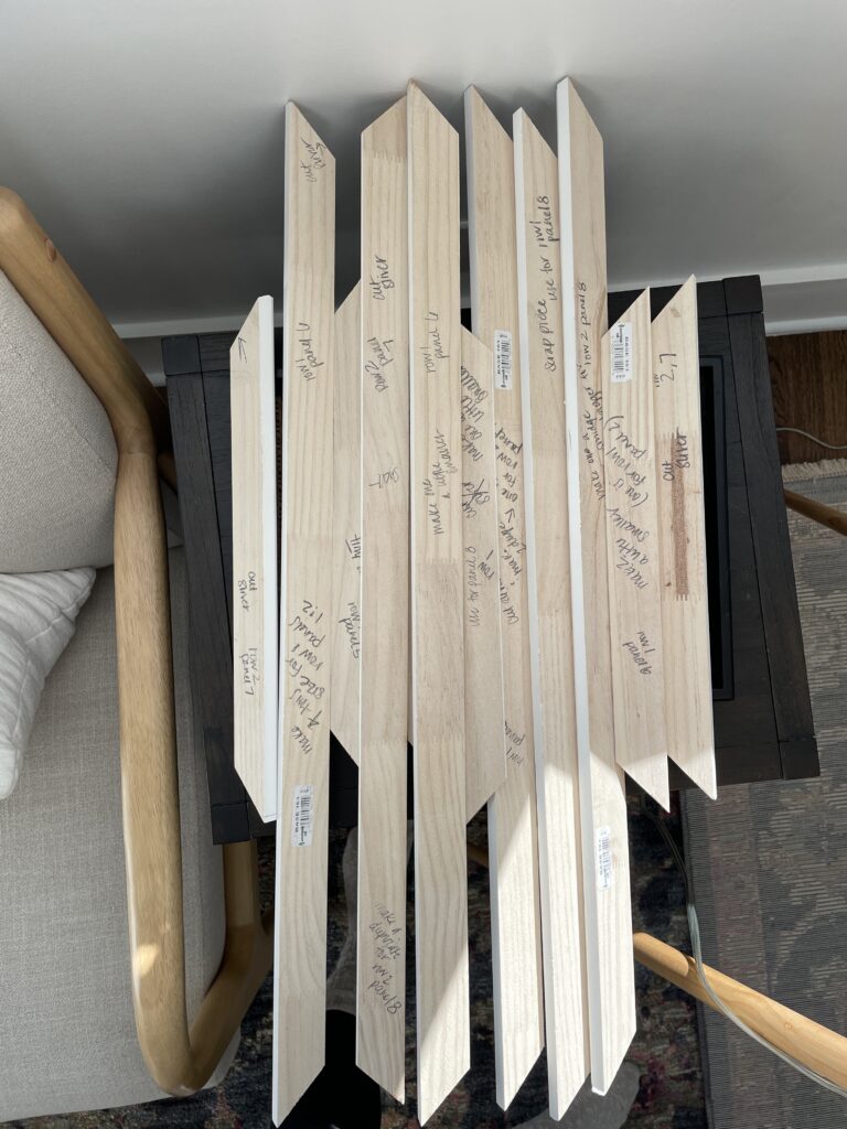 Elisha from Our Aesthetic Abode is showing how she marked notes on her trim pieces for her Recessed Wainscoting Accent Wall. These notes say things like "cut 1/8" shorter" or "make a duplicate of this piece"