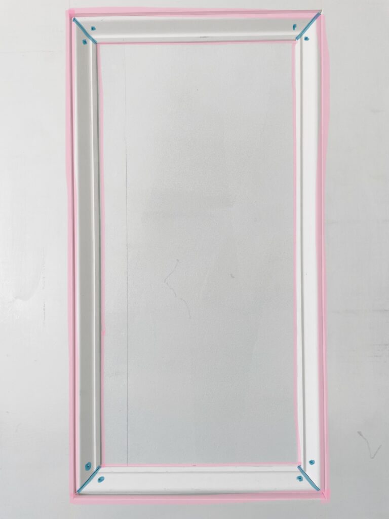 Elisha from Our Aesthetic Abode is showing a photo of a panel of the Recessed Wainscoting Accent Wall. The photo shows where she caulked vs where she used spackle (caulk lines are shown in pink and spackle in blue)