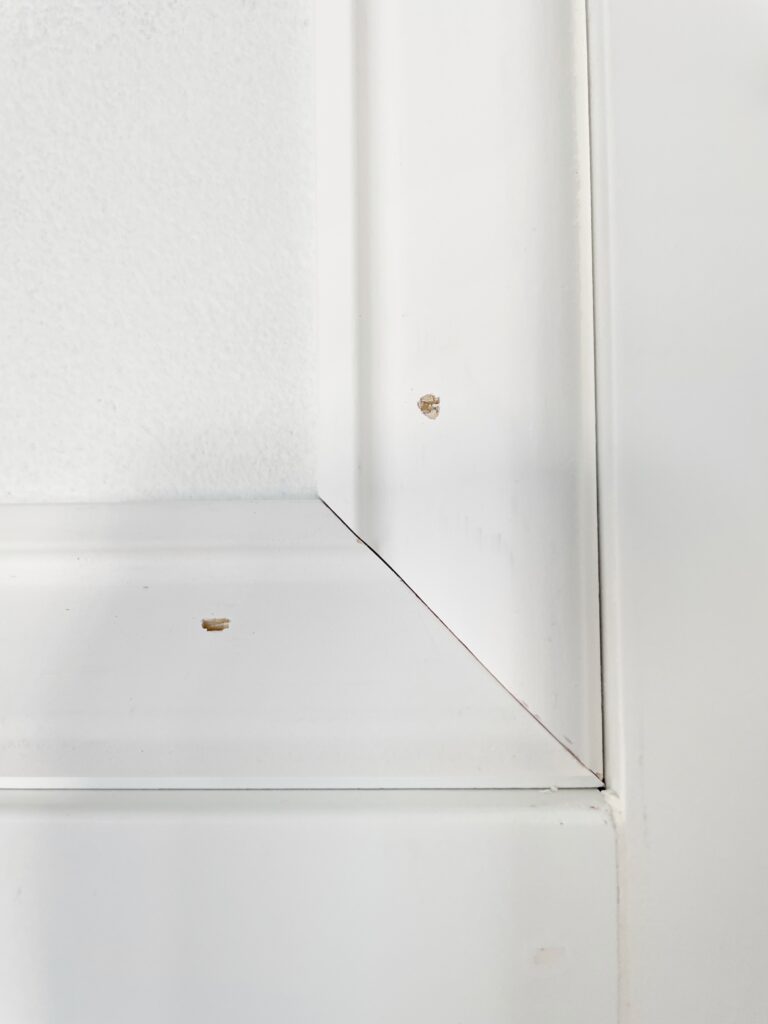 Elisha from Our Aesthetic Abode is showing an up close view of the trim pieces for her Recessed Wainscoting Accent Wall. The photo shows where the angled trim pieces meet as well as the where the nail holes are.