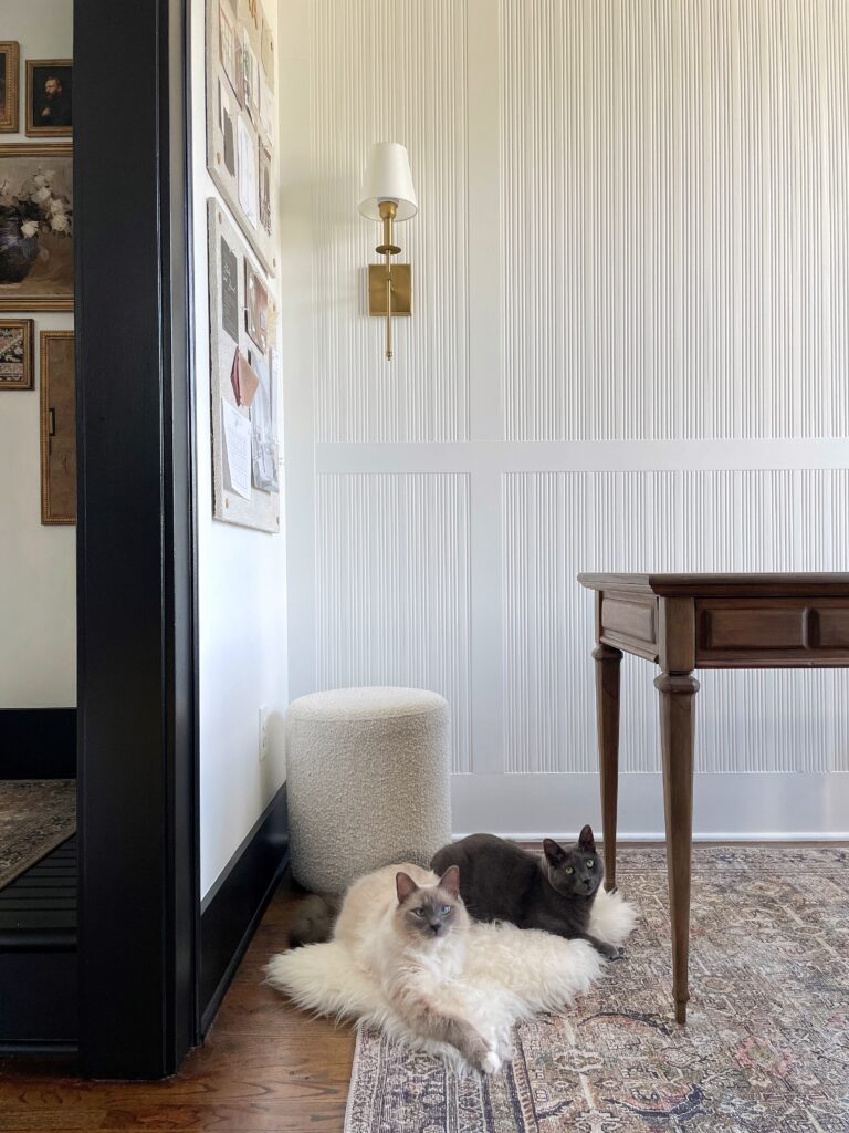 A view of a fluted accent wall, black trim and a partial view of black painted stairs, and two cats laying on the floor