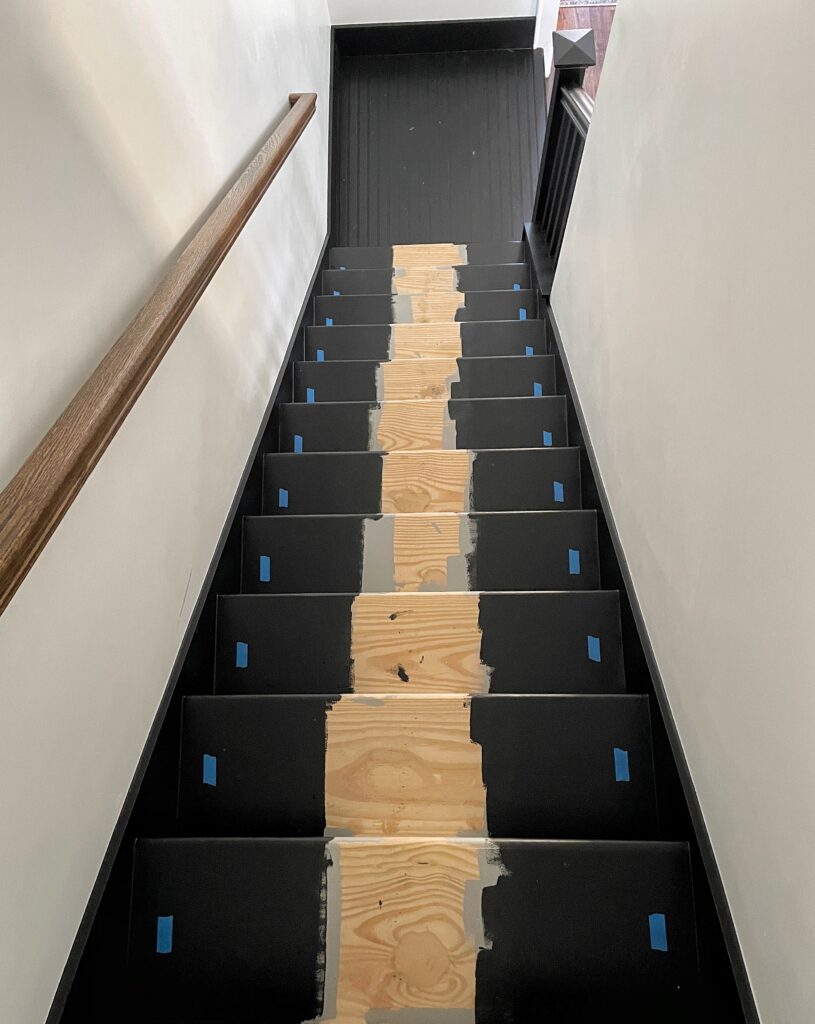 black painted stairs with blue painter's tape marking the placement of the runner