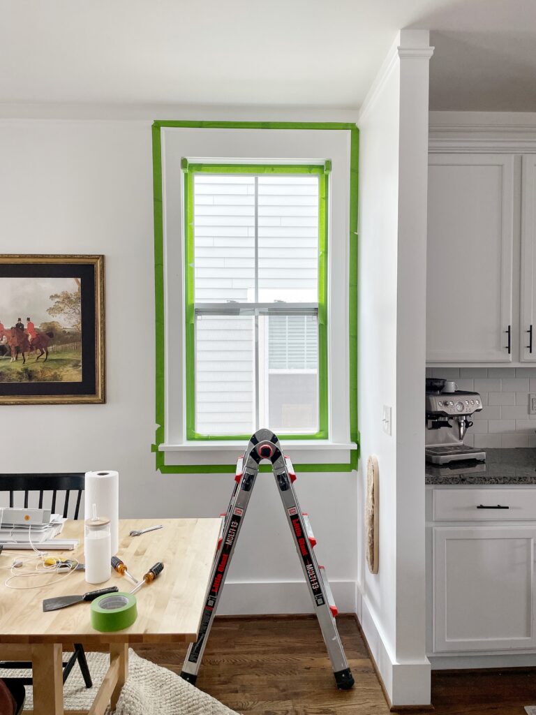 a window that's taped off with green painter's tape in preparation for paint