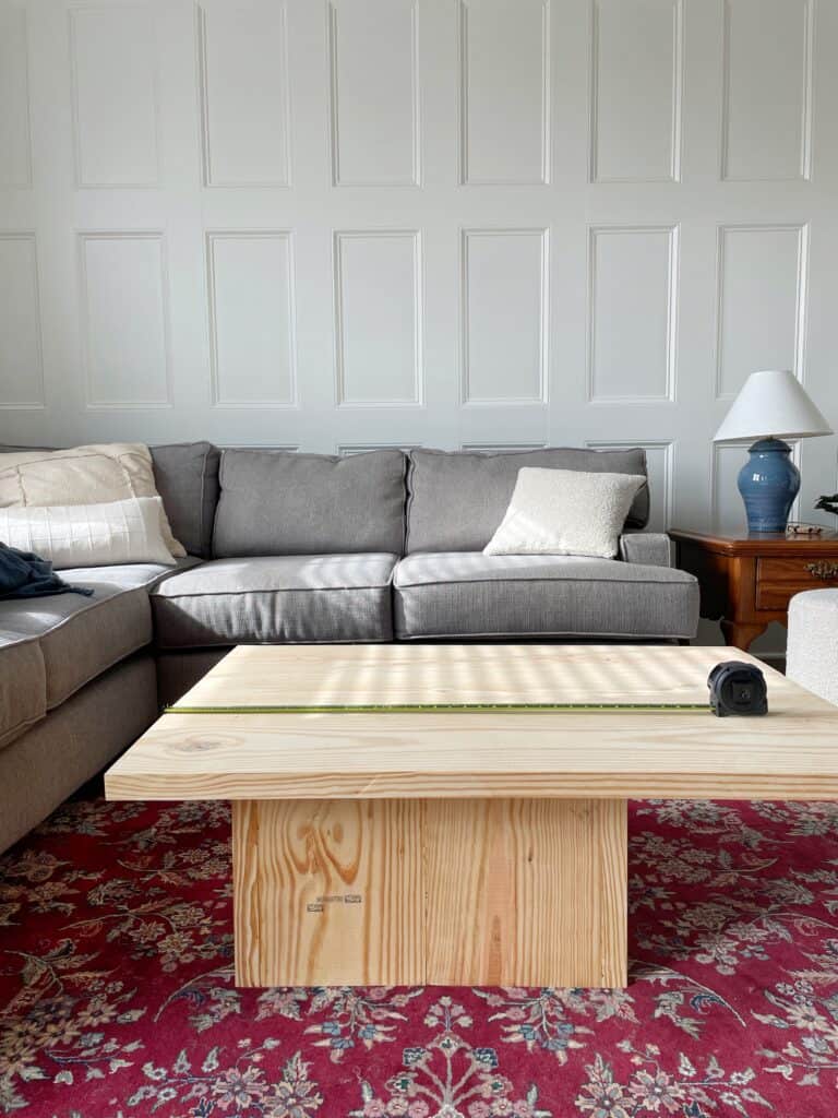 A DIY wood coffee table with measuring tape over the top to determine what size to cut it