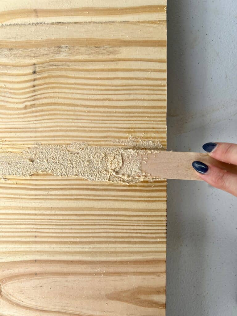Homemade wood filler is being applied to pine with a popsicle stick for a diy coffee table