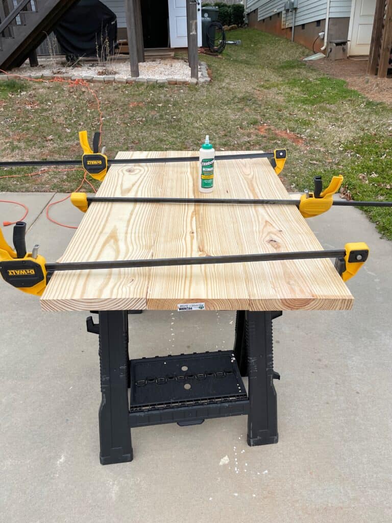 3 large clamps are being used to hold together pieces of pine for a diy modern coffee table