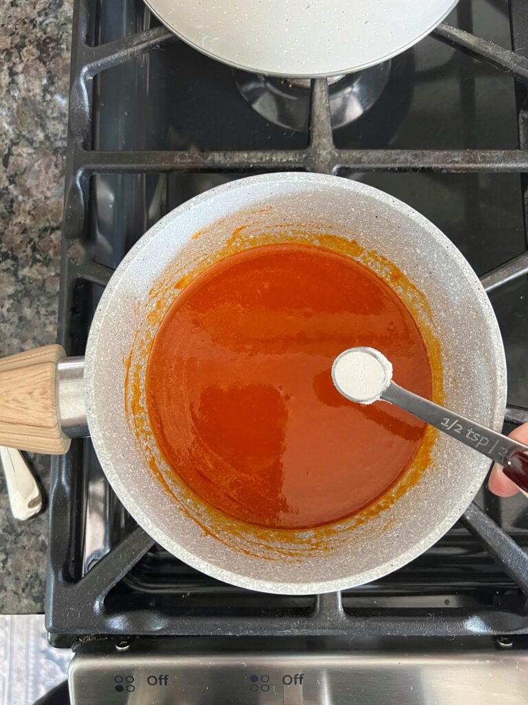 A saucepan with homemade buffalo sauce and a 1/2 tsp of flour about to go in