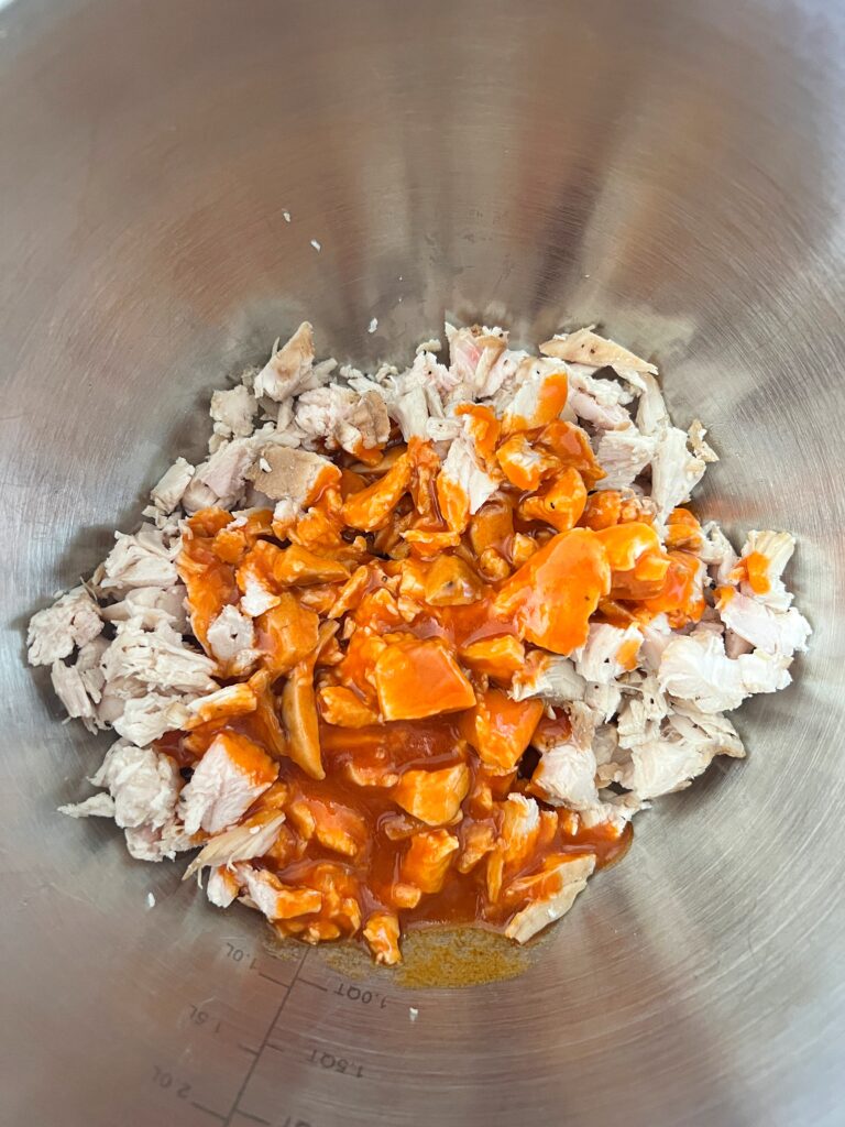 A bowl of shredded chicken with buffalo sauce for buffalo chicken egg rolls