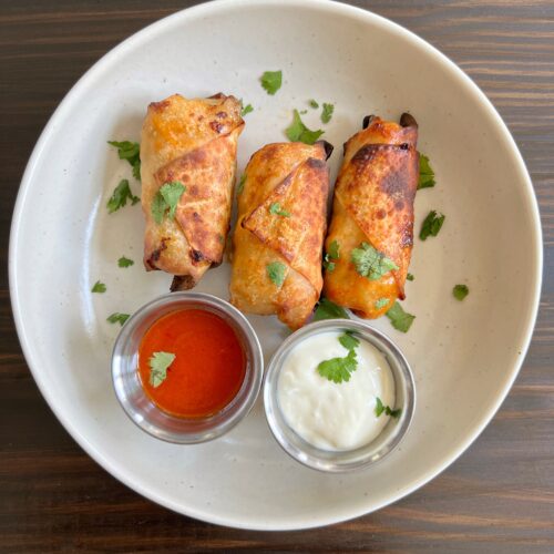 Three healthy air fryer buffalo chicken egg rolls with a side of buffalo sauce and blue cheese