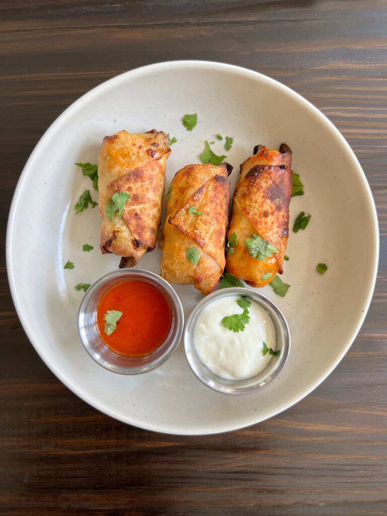 Three healthy air fryer buffalo chicken egg rolls with a side of buffalo sauce and blue cheese