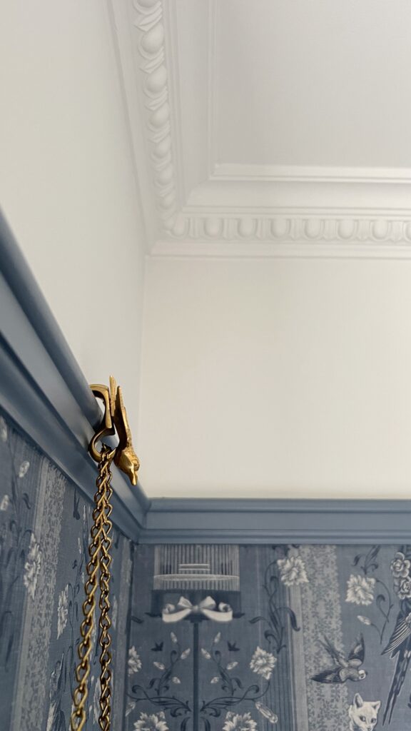 a brass bird hook used with chain to hang photos off of picture rail trim