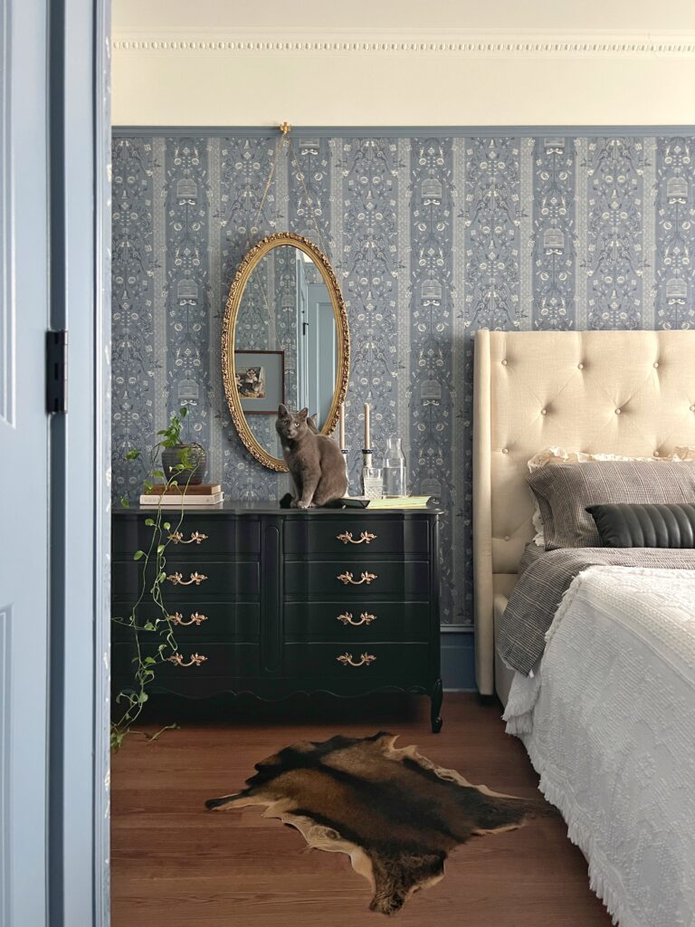 blue floral wallpapered bedroom with a black french provincial dresser and vintage and cowhide rug
